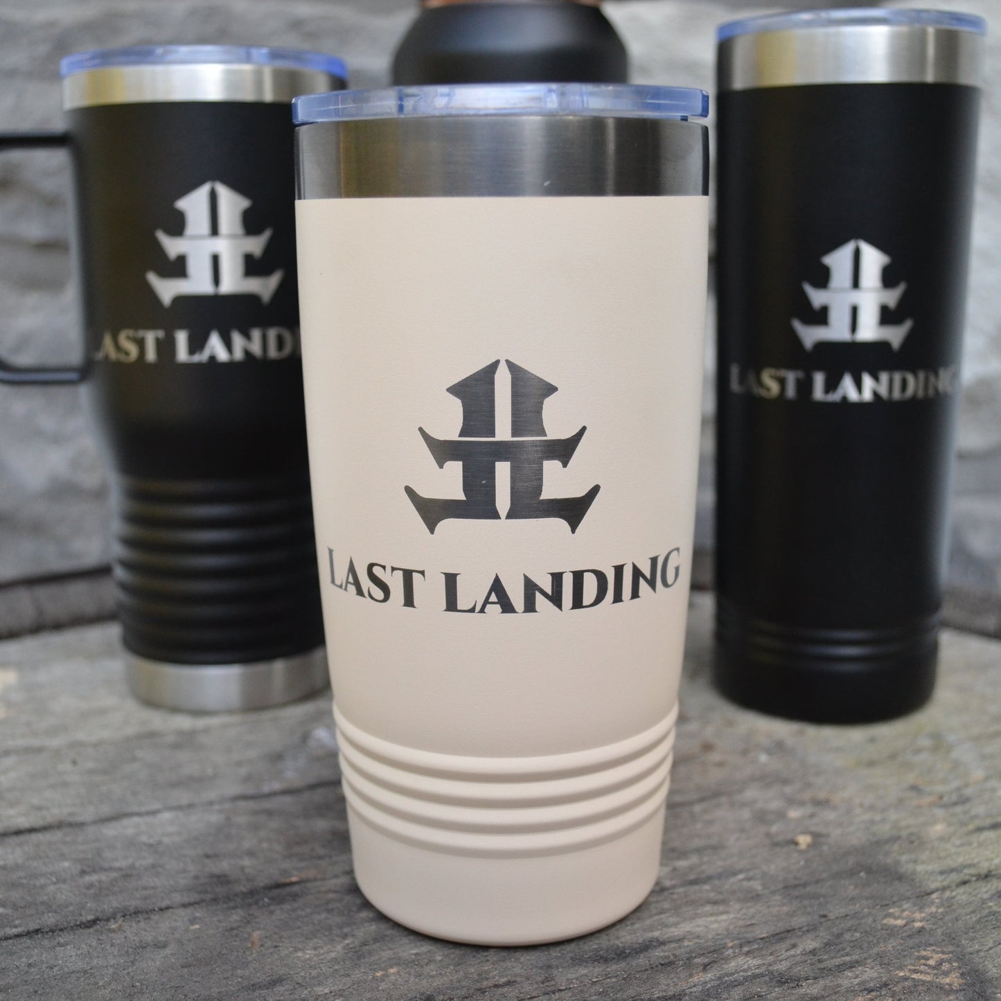 Travel mugs with 'Last Landing' logo on a wooden surface