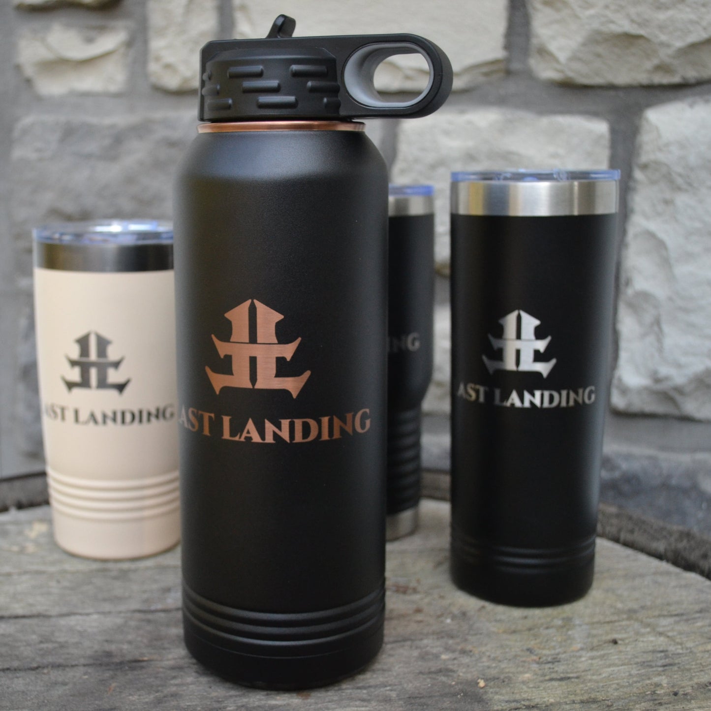 Black and beige insulated cups with 'West Landing' logo on a stone surface.