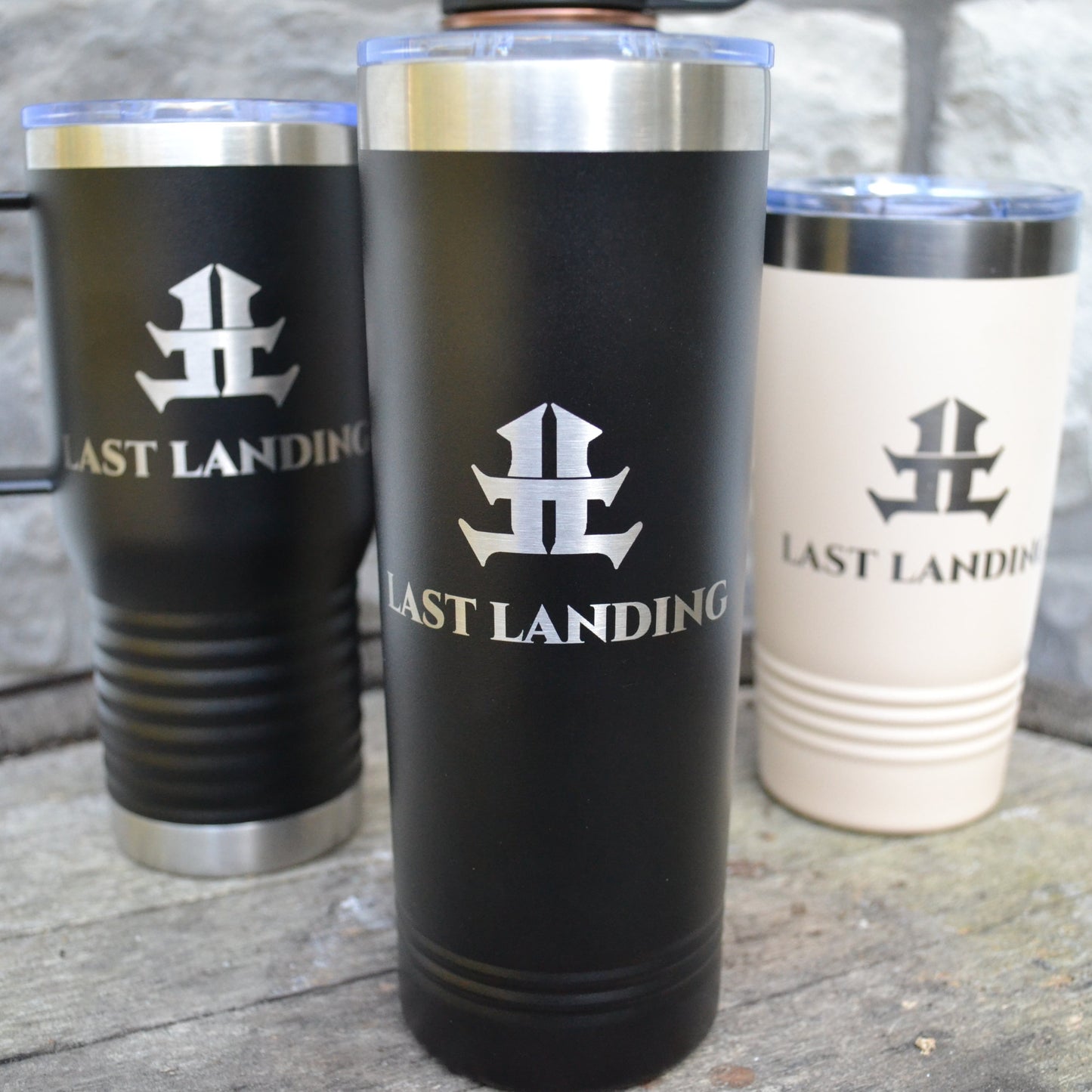 Three insulated travel mugs with 'Last Landing' logo on a wooden surface.