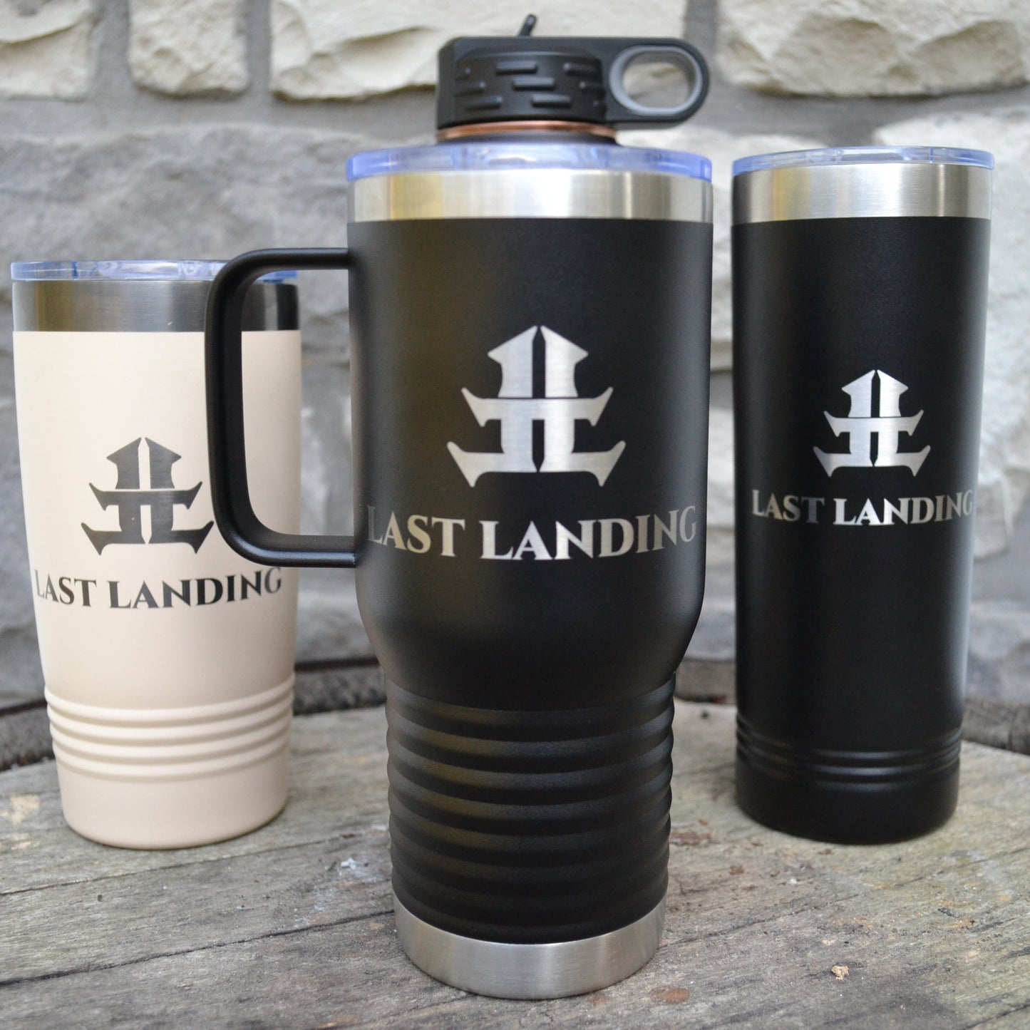 Three insulated travel mugs with 'Last Landing' logo on a wooden surface.