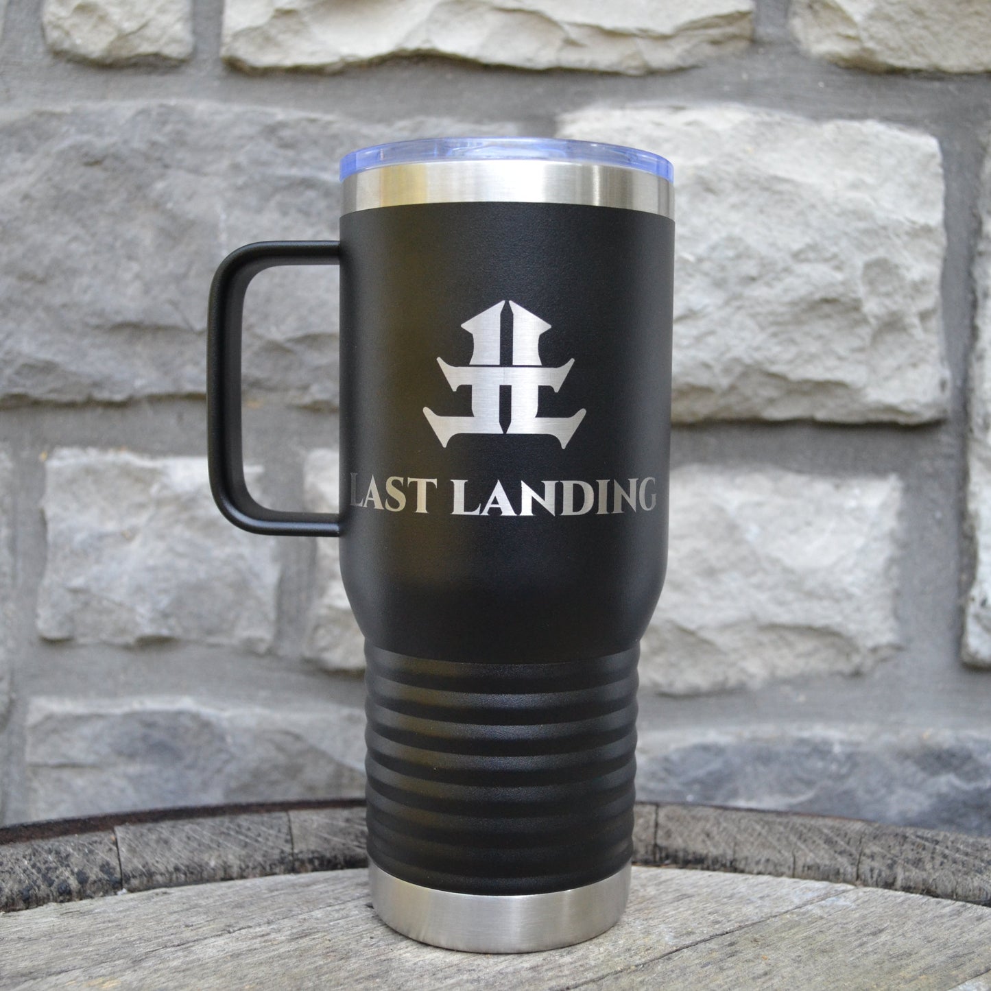 Black travel mug with 'Last Landing' logo against a stone wall background