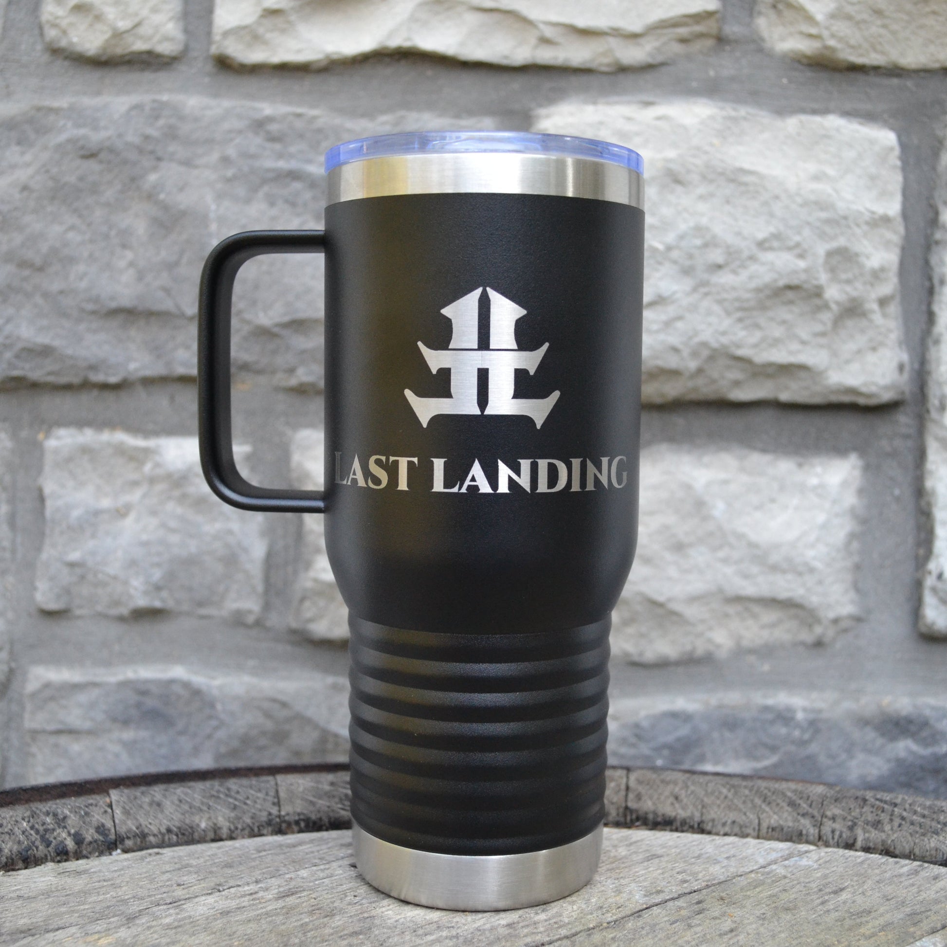 Black travel mug with 'Last Landing' logo against a stone wall background