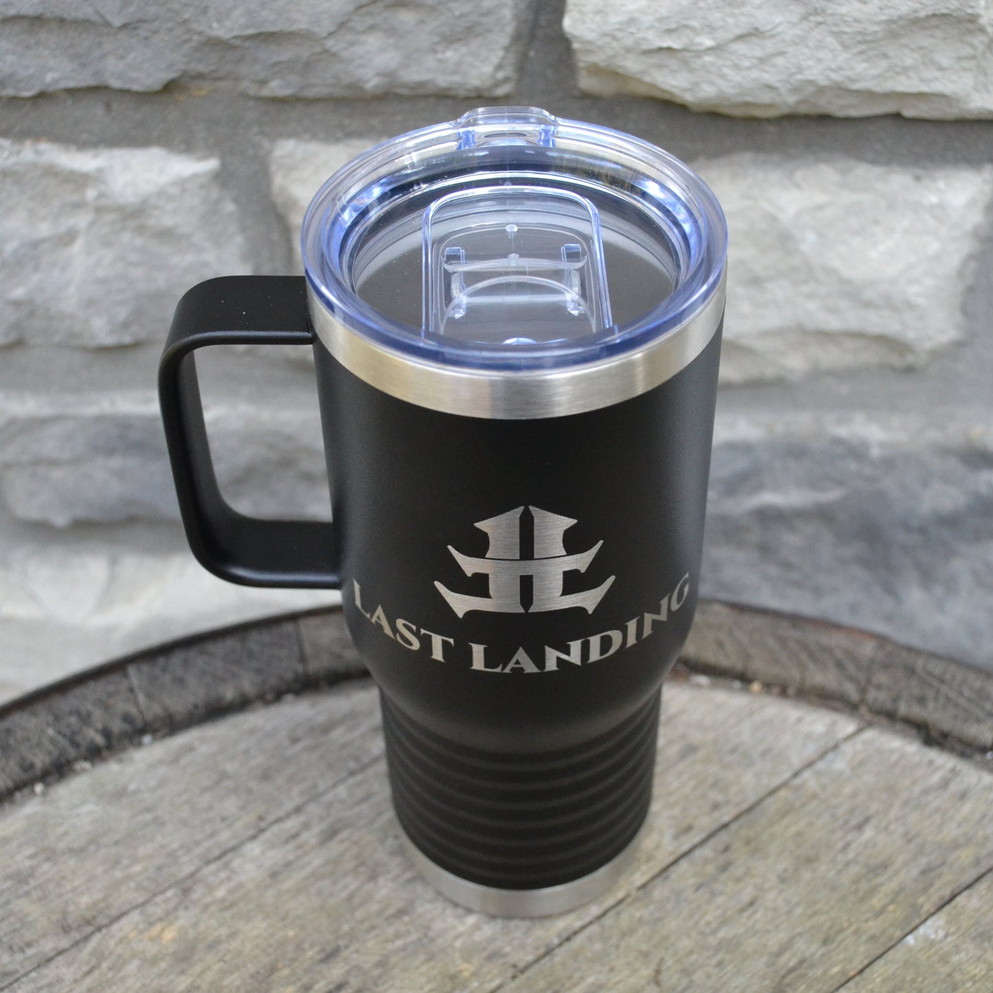 Black travel mug with a logo on a stone surface