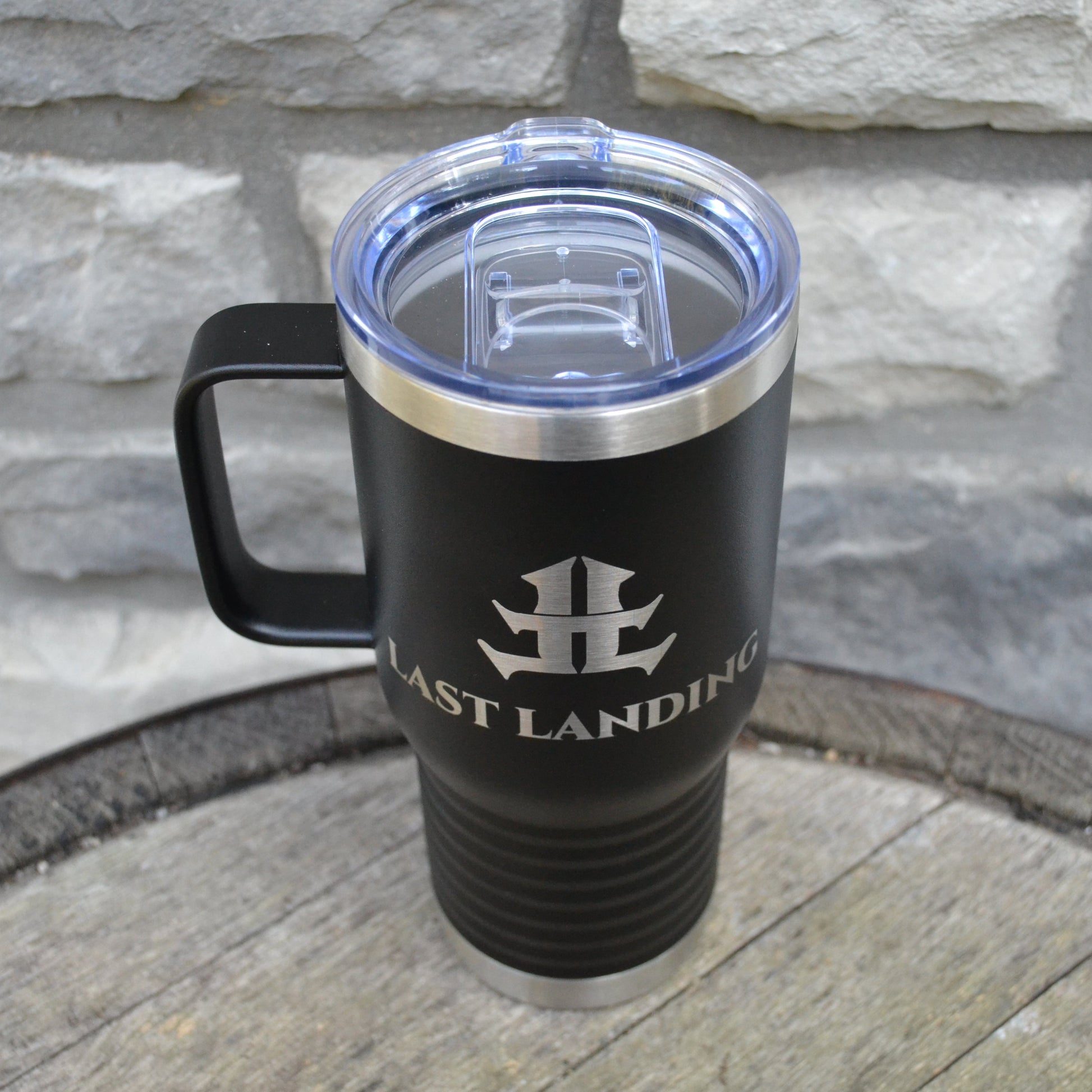 Black travel mug with a logo on a stone surface