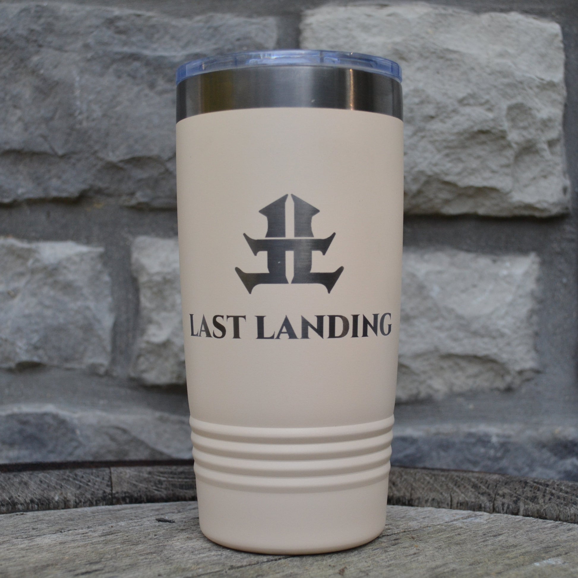 Beige tumbler with 'Last Landing' logo against a stone wall background