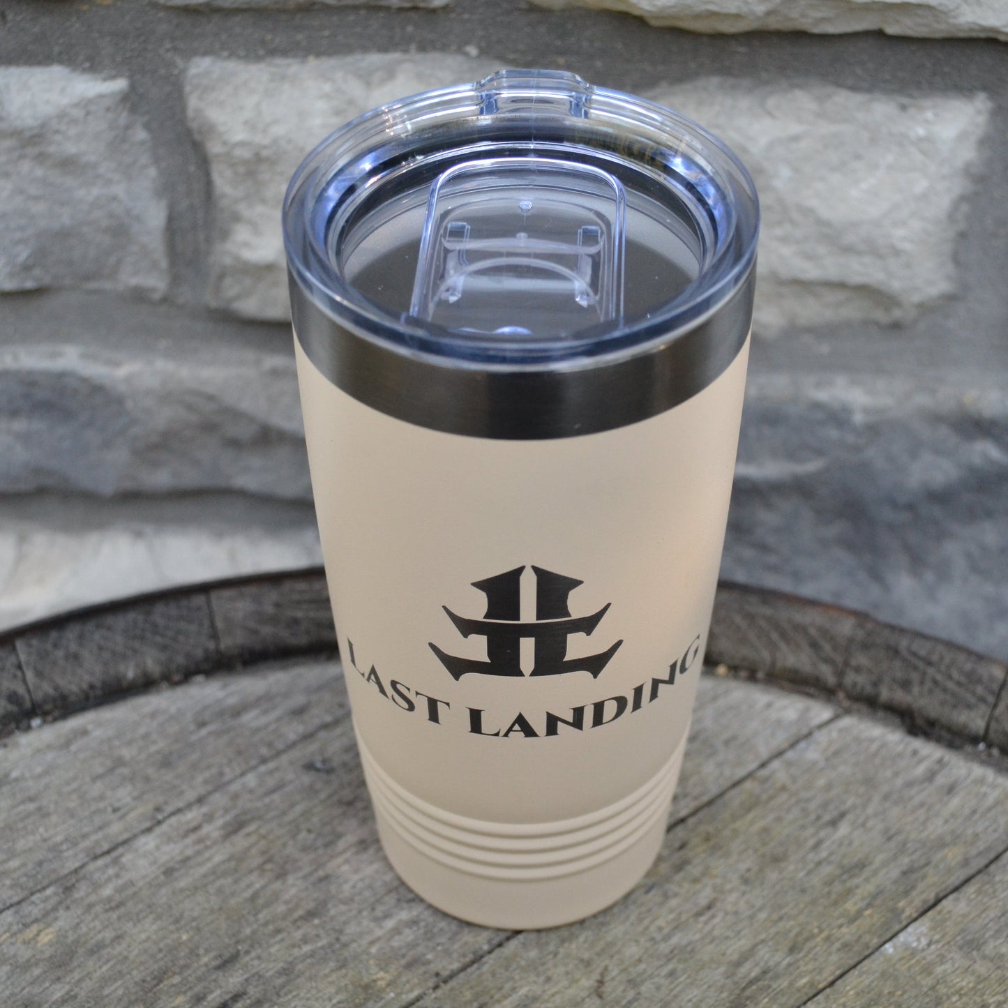 Beige tumbler with black logo and text on a stone surface