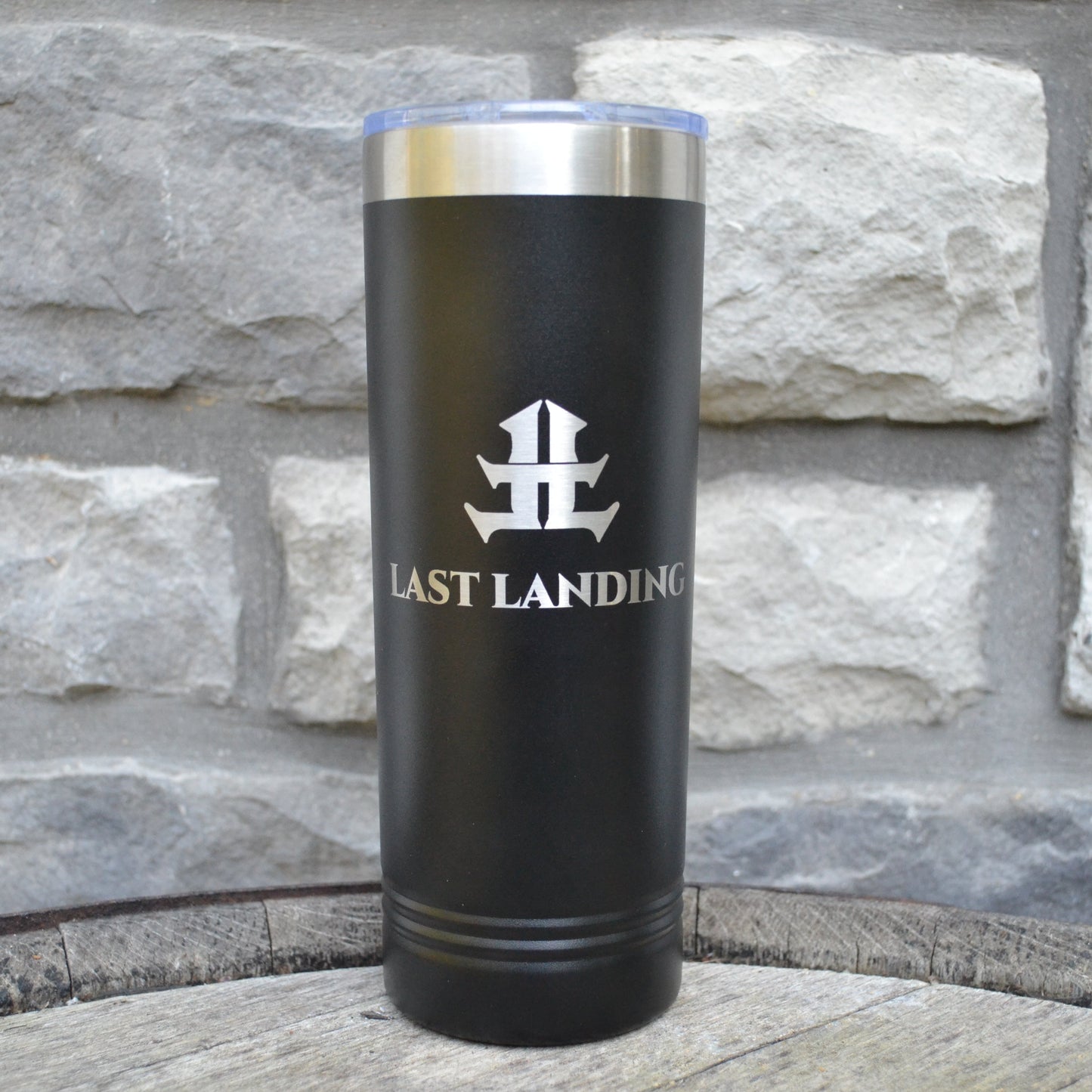 Black tumbler with 'Last Landing' logo on a stone surface